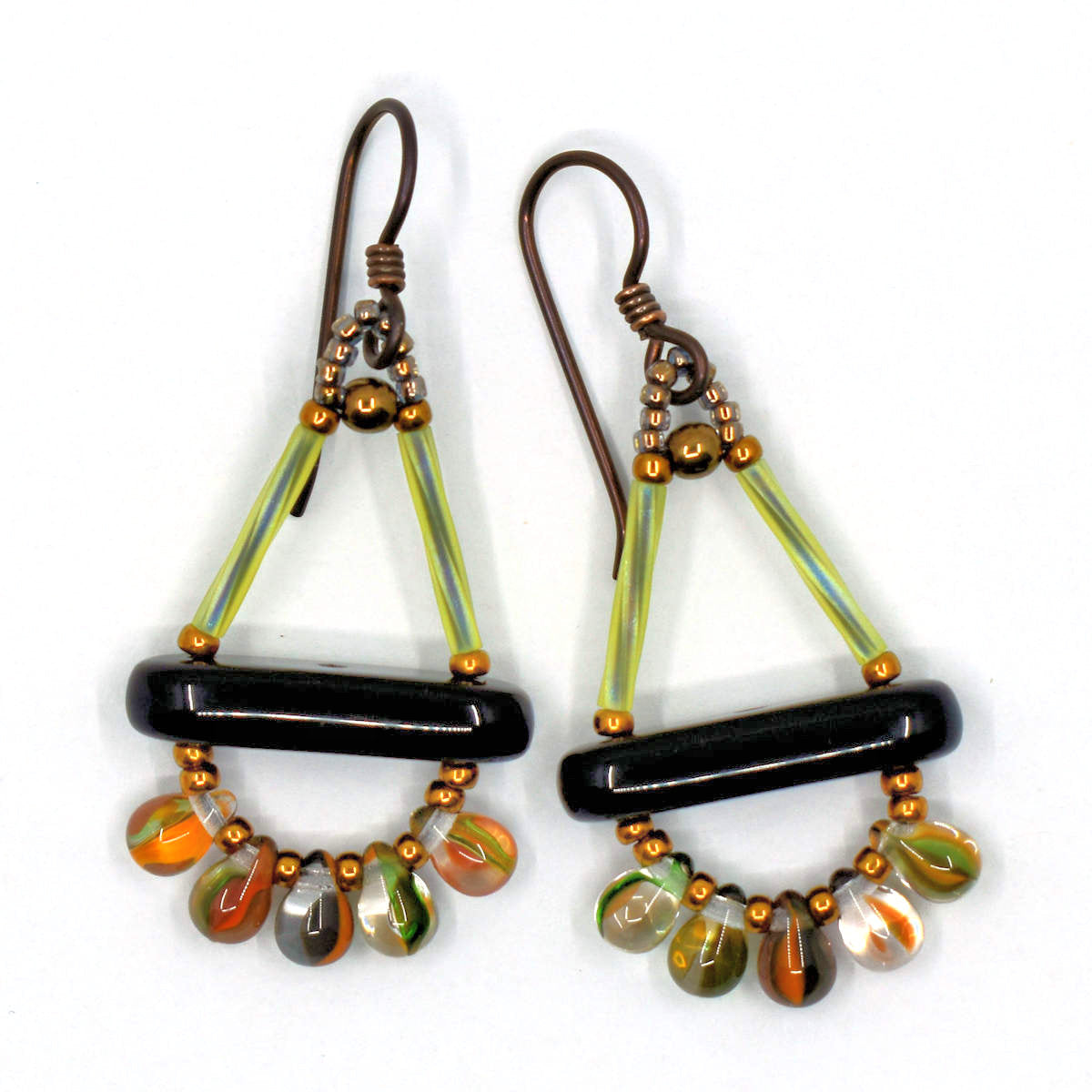 A pair of earrings with a spray of colorful drops at the bottom lays on a white background. The earrings have a triangle shape at the top formed by two light green upright sides and a black bar at the bottom. Below the bar is a swag of five drop beads, each clear with a variety of autumn colored stripes inside of it.. 