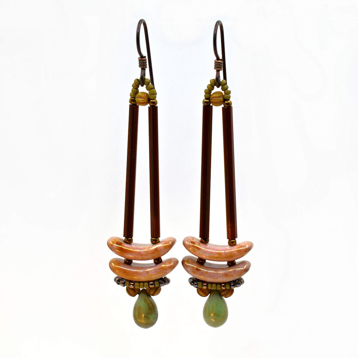 Earrings that look similar to a medicine dropper lay on a white backround. There are two long, brown beads forming narrow vertical columns ending at the top of two speckled pink stacked arc shaped beads. At the bottom is a matte speckled turquoise green drop shaped bead, surrounded by a belt of matte gold seed beads.