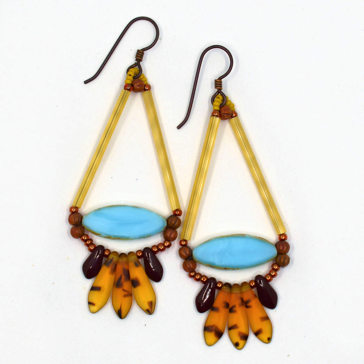 Long gold and amber earrings shaped like a teardrop with a wide light blue pointy oval at the base lay on a white background. At the bottom of the earrings' teardrop shape is a fan of five dagger beads, three transparent amber tortoiseshell in the center, sandwiched between two smaller dark brown daggers. The earrings have dark ear wires.