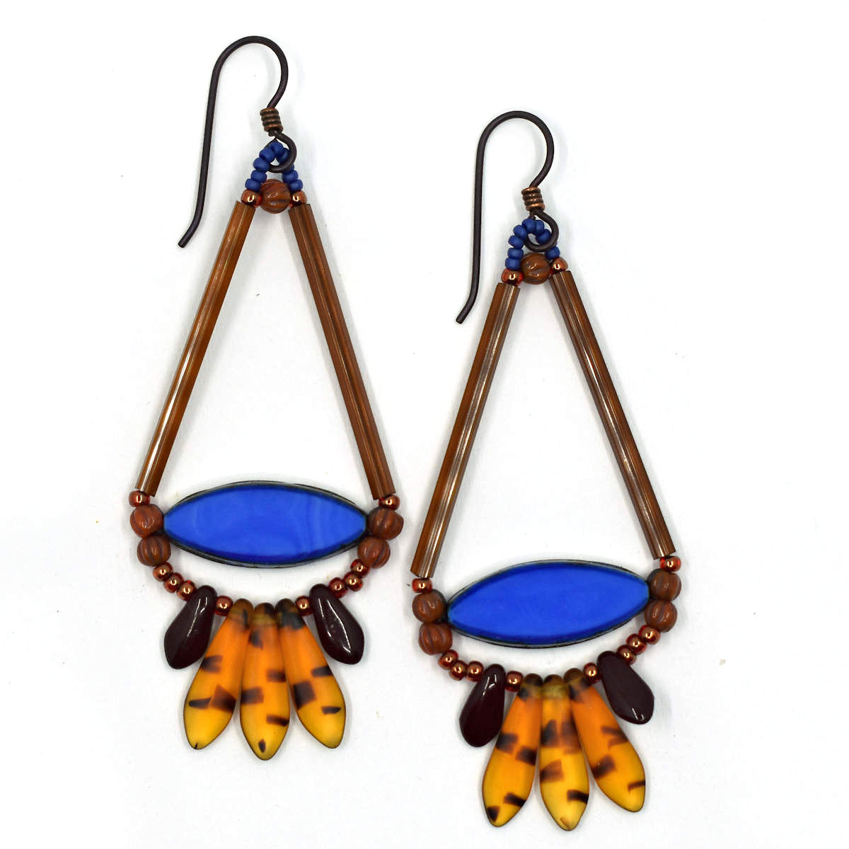 Long gold and amber earrings shaped like a teardrop with a wide medium blue pointy oval at the base lay on a white background. At the bottom of the earrings' teardrop shape is a fan of five dagger beads, three transparent amber tortoiseshell in the center, sandwiched between two smaller dark brown daggers. The earrings have dark ear wires.