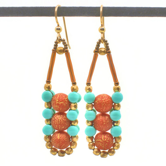 Gold-dusted coral red and turquoise earrings with gold accents and ear wires hang from a black bar against a white background. These earrings have a vertical stack of coral colored beads with a rough, gold antiqued finish. They are held together by an outline of alternating turquoise and gold beads. 