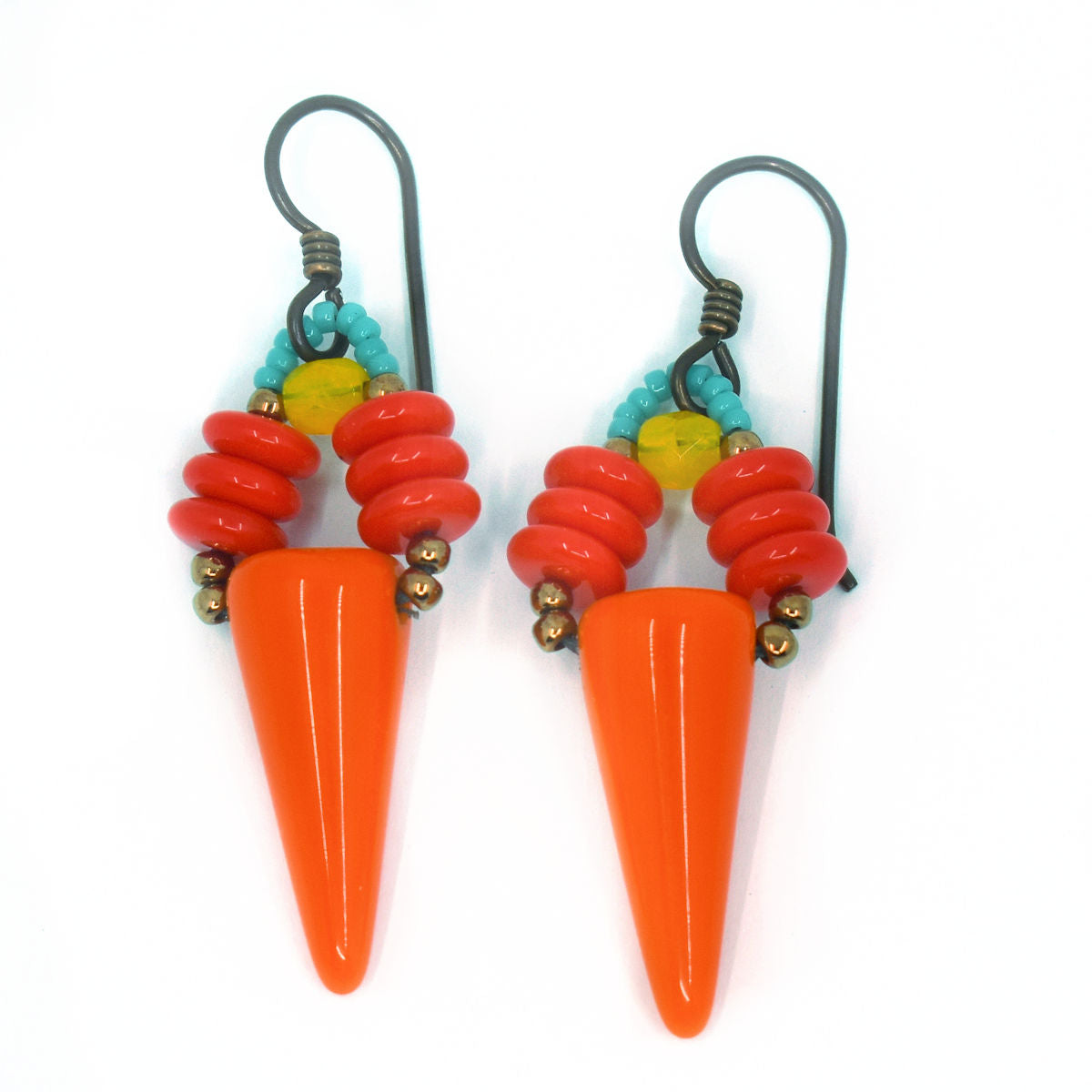 A pair of brightly colored earrings laying on a white background. The earrings have an upturned orange cone suspended from two parallel stacks of red discs and turquoise and yellow accents.