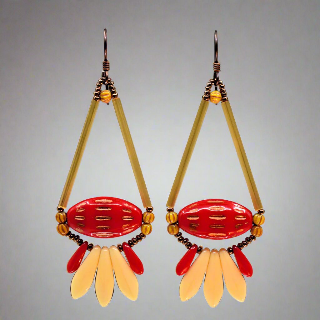 Long red and cream earrings shaped like teardrops with a tail feathe against a gray background. The earrings have dark wires and are formed from two long yellow-gold tube beads that form the top of a teardrop with a wide glossy red oval with pointed ends and horizontally running copper dash marks. Below the teardrop shape is a fan of three cream dagger beads sandwiched between two smaller red daggers. The earrings have dark ear wires.