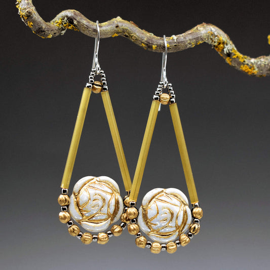Long gold and white earrings shaped like open teardrops with gold embossed rose-shaped beads in the round base. Below the roses is an outline formed from small gold beads alternating with silver seed beads. The earrings have silver ear wires.